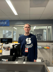 Blonde boy in Penn State shirt, smiling and working at the cash register at the Penn State Bookstore
